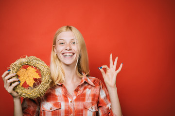 Autumnal mood. Decorative autumnal wreath with maple leaf. Smiling woman in plaid shirt with wreath. Autumn sale. Happy girl with autumn wreath shows ok sign. Autumn fashion. Copy space for advertise.