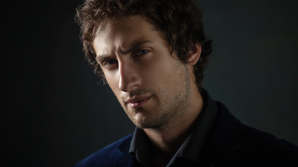Obraz premium Handsome young brunette man with light eyes in dark clothes looks into the distance.