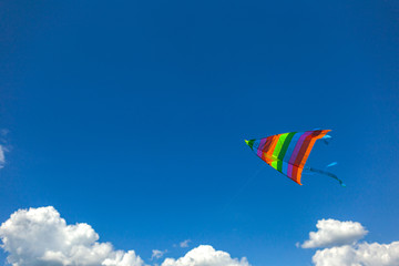 Colourful small kite flying in bluy sunny bright sky. Horizontal color photography.