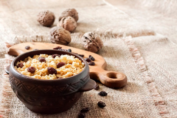 Sweet millet porridge with dark raisins in ceramic rustic bowl with walnuts in background