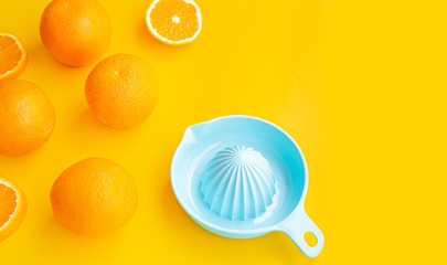 Perspective view fresh orange slices and blue juicer on summer yellow background with copy space