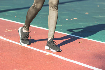 Woman in sneakers and sport clothes makes sport exercises on the athletic field, blurred background