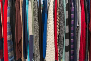 Row of colourful tone of knitted crocheted sweater and jumper hang on aluminium hanger clothes rack in retail fashion store or second hand outlet shop.
