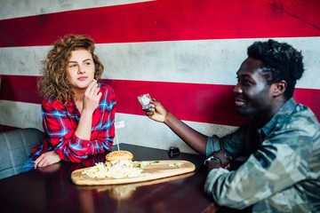 Loving couple  ar eating burgersin modern, supper  cafe with african flag.