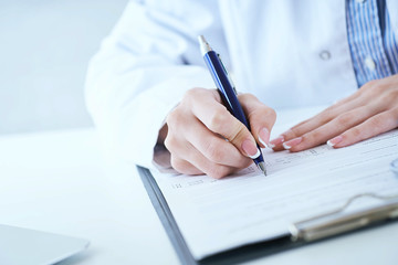 Fototapeta premium Female medicine doctor hand holding silver pen writing something on clipboard closeup. Lot of paper work in medicine. Ward round, patient visit check, medical calculation and statistics concept.