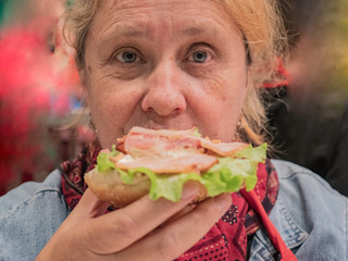 Retired elderly woman with red hair is tasting large hamburger cooked in high-tech kitchen. Master class on cooking meat dishes and hamburgers