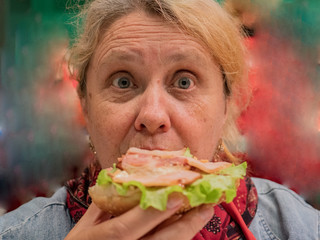 Retired elderly woman with red hair is tasting large hamburger cooked in high-tech kitchen. Master class on cooking meat dishes and hamburgers