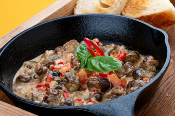 Fried snails in cream sauce, in a cast iron pan. On a wooden stand.