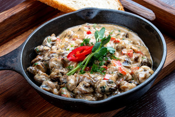 Fried snails in cream sauce, in a cast iron pan. On a wooden stand.