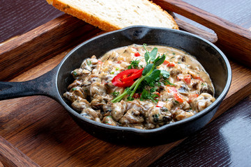 Fried snails in cream sauce, in a cast iron pan. On a wooden stand.