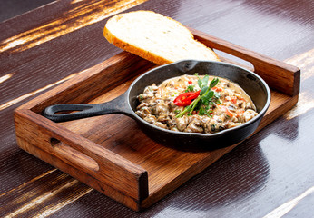 Fried snails in cream sauce, in a cast iron pan. On a wooden stand.
