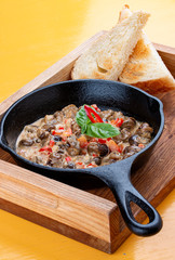 Fried snails in cream sauce, in a cast iron pan. On a wooden stand.