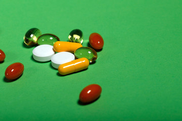 A lot of bright pills of drugs on a green background. Cropped shot, horizontal, side view. The concept of medicine and health. Crisis opioid painkiller and drug addiction concept.