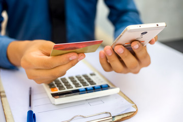 Fototapeta premium Close up of employee holding a smart cell phone and credit card in his hand wearing a blue colored shirt and black necktie. Concept of banking and shopping isolated on white.