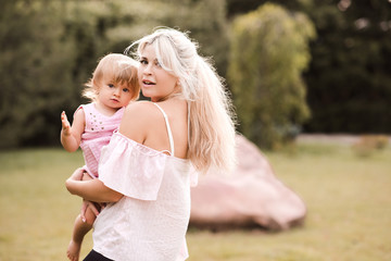 Beautiful mother holing baby girl 1 year old posing in park outdoors. Looking at camera. Motherhood.