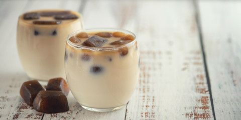 Milk coffee cocktail in glasses with frozen coffee cubes on light wooden table. With copy space