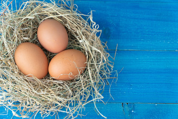 Fresh brown chicken eggs in hay nest on blue wooden background. Concept of organic eggs, free space for text or other elements
