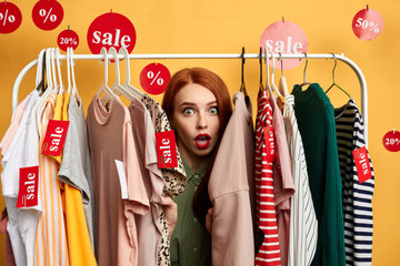 surprised girl hiding among clothes on hangers woman is being surprised after hearing the prizes of clothes. unbelievable sale. trade. close up photo. - obrazy, fototapety, plakaty
