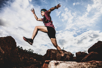 side view of trail runner jumping on the horizon and stone