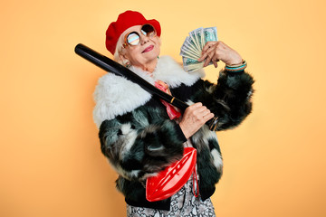 romantic rich woman with a bat on her shoulder using her money like a fan. isolated yellow background. studio shot.
