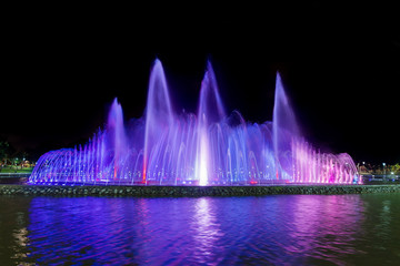 Colorful luminous and musical fountain. Night view. Multicolored streams of water are blurred against a black sky.
