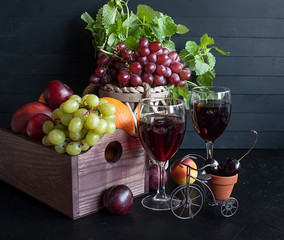 Two glasses of red wine, grapes, fruit on a black wooden table.