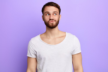 Young funny bearded attractive mman with skeptic look, has some doubts, looks aside, isolated over blue background. close up portrait. place for text. copy space