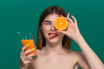 Closeup portrait of beautiful young woman with bright color make-up holding orange juice and biting half of an orange