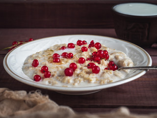 Breakfast of oatmeal porridge with fresh berries of currants and milk, shot from close range