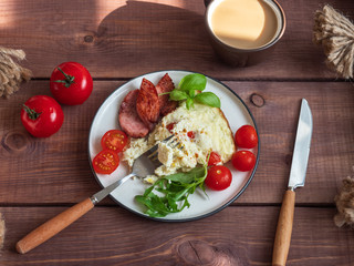 Breakfast of omelet with fried sausage and fresh tomatoes, and arugula and basil, coffee with milk in a ceramic mug