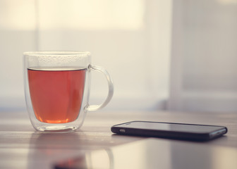 Transparent cup of tea, phone, tablet on a white wooden table.