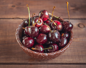 Ripe large sweet cherries in a deep ceramic brown bowl on an wooden tray
