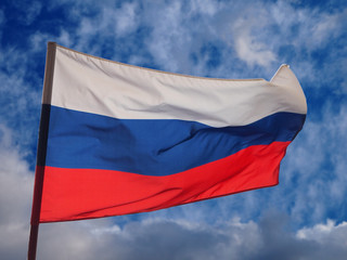 The national flag of the Russian Federation waving in the wind on the thunderclouds and blue sky background
