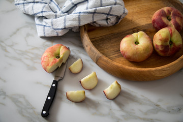 Plattpfirsiche mit Messer und Geschirrtuch in Holz Schale auf Küchen Marmor Tisch