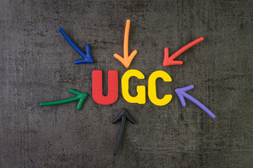 UGC, User generated content using in brand communication online advertising concept, multi color arrows pointing to the word UGC at the center of black cement chalkboard wall