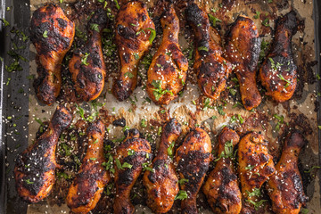 Obraz na płótnie Canvas Grilled hicken legs BBQ with spices herbs and sesame on baked paper - Top of View. Roasted poultry meal in roaster dish