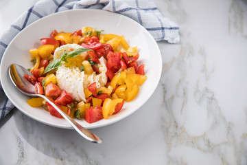 Mozzarella Kugel mit roten und gelben Tomaten, Basilikum und Olivenöl auf Teller auf Marmor Hintergrund