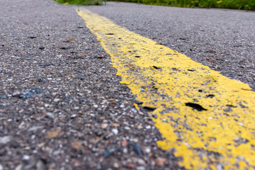 Yellow solid line, grunge single road marking on asphalt close up, background with copy space
