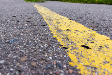 Obraz premium Yellow solid line, grunge single road marking on asphalt close up, background with copy space