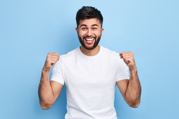 excited Arab man celebrating success with two fists in air isolated on the blue background. close...