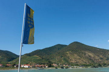 Flag of the country Lower Austria in the Wachau in front of the Danube with a mountain with vineyards in the background