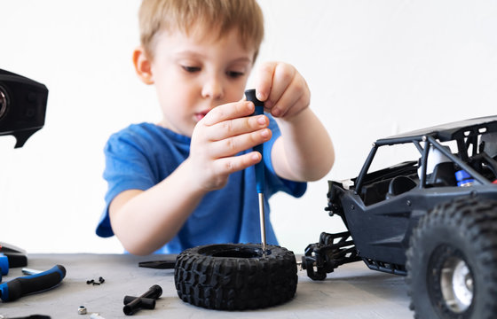 obby radio modeling: a little boy in a blue T-shirt repairing a radio-controlled car buggy with a screwdriver.
