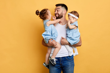 Young happy father holding his his little daughters in hands isolated yellow background. close up...