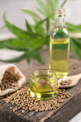 Obraz na płótnie Canvas CBD oil. Hemp oil in two glass jar and bottle with grain in the sack on wooden board with leaves of cannabis on background.