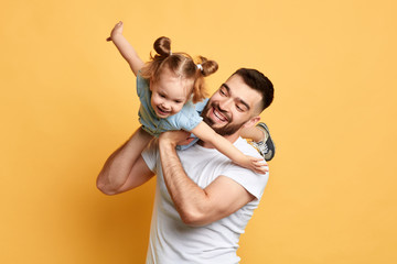 cheerful happy man teaching sweet lovely daughter to fly like a plane. close up photo. isolated yellow background. studio shot, happy moments with best father - 280888828