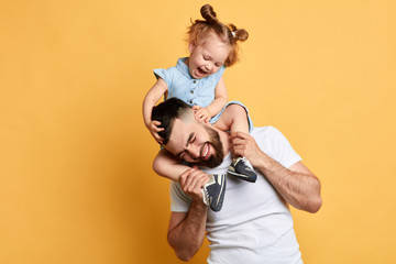 little lovely girl tickling her daddy while sitting on his shoulders . isolated yellow background, studio shot.feeling and emotion