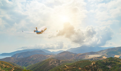 Fototapeta na wymiar White passenger plane in flight. The plane flies against a background of mountain landscape. Aircraft rear view.
