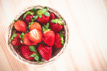 Top view of a wicker basket filled to the top with fresh strawberries on a wooden table. Delicious first class organic fruit as a concept of summer vitamins. Healthy sweet food. With copy space.