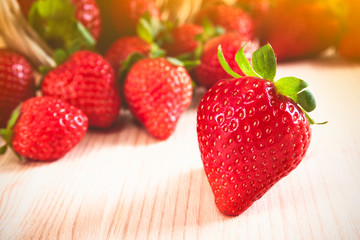 Closeup to fresh strawberries falling on a wooden table and illuminated by sunlight. Delicious first class organic fruit as a concept of summer vitamins. Healthy sweet food. Food background.