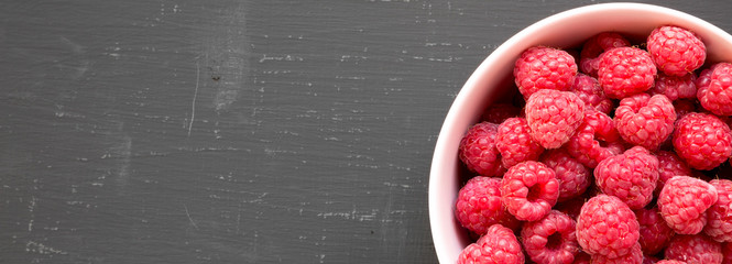 Raw raspberries in a pink bowl on a black surface, top view. Healthy eating and dieting. From...